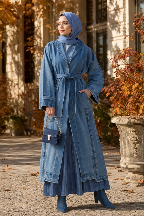 Blue Denim Layered Outfit A woman wears a blue belted denim coat over a long pleated blue skirt with a matching hijab, ankle boots, and a small chain-strap handbag.