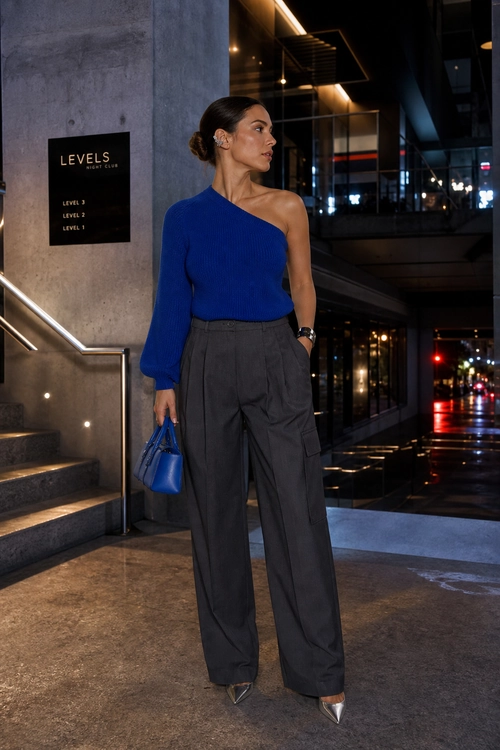 A blue one-shoulder knit top is styled with charcoal wide-leg trousers, a blue handbag, and pointed silver heels.