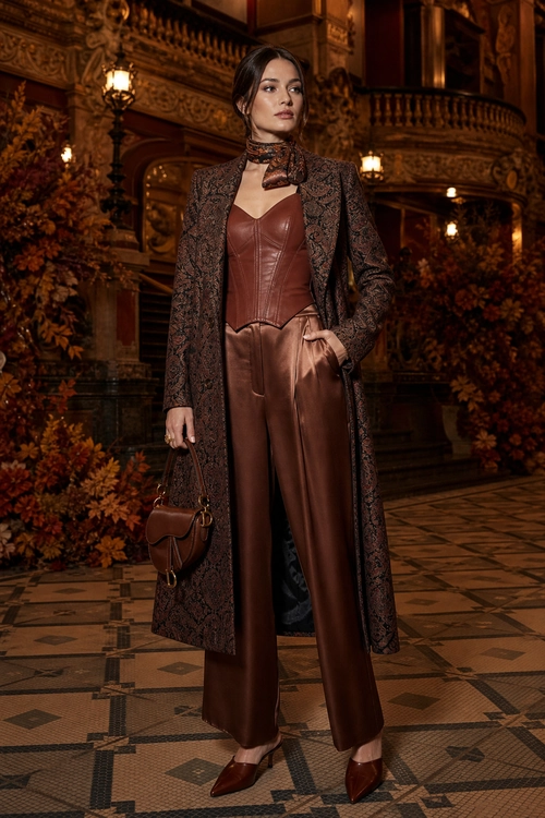 Brown Leather-Look Tailored Outfit A woman wears a long patterned brown coat over a brown leather-look top and wide-leg trousers, styled with a neck scarf, handbag, and pointed shoes.