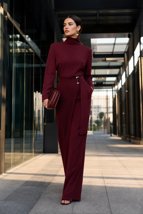 Burgundy Tailored Jumpsuit Look A woman wears a burgundy long-sleeve high-neck jumpsuit with a waist sash, clutch, hoop earrings, and open-toe sandals.