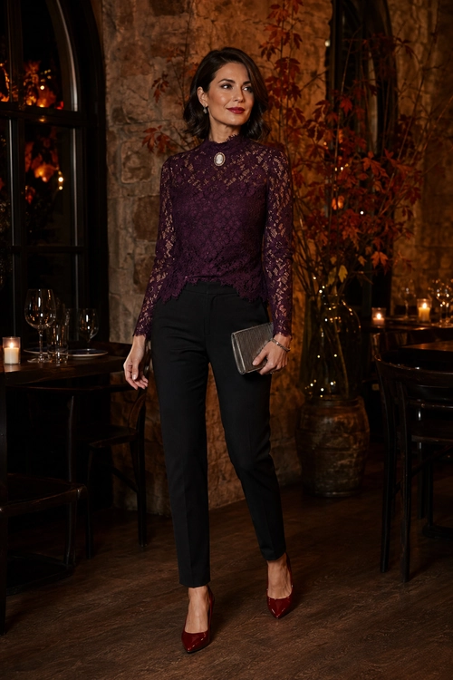 Burgundy Lace Top and Black Trousers A woman wears a burgundy lace long-sleeve top with black trousers, pointed burgundy heels, and a metallic clutch.