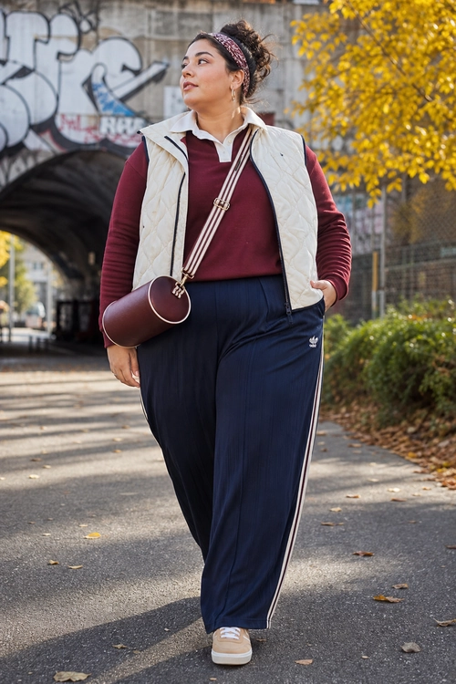 A burgundy collared top, cream quilted vest, navy striped track pants, white sneakers, and a burgundy crossbody bag create a casual athleisure outfit.
