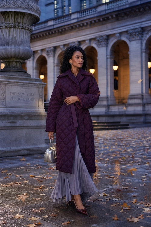 Burgundy Quilted Coat with Pleated Skirt Woman wearing a burgundy quilted belted coat over a gray pleated skirt with burgundy pointed shoes and a small metallic handbag.