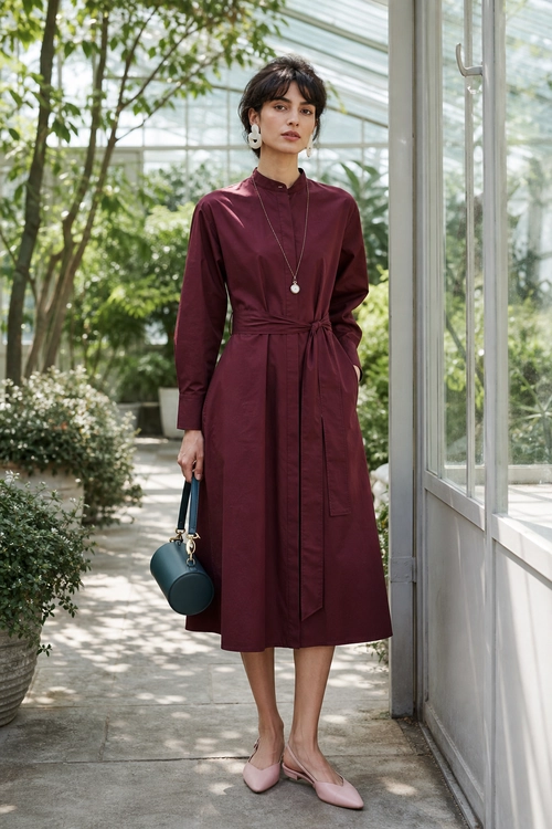 Burgundy Tie-Waist Midi Dress Woman wearing a burgundy long-sleeve tie-waist midi dress with pink pointed flats and a teal round handbag.
