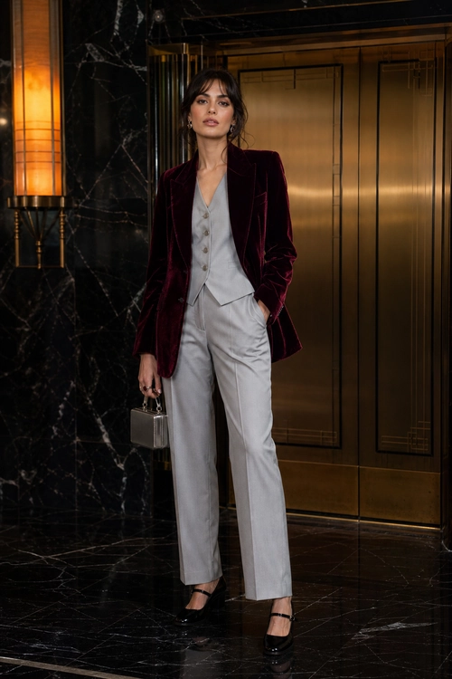 Burgundy Velvet Blazer with Gray Tailoring A tailored outfit featuring a burgundy velvet blazer, light gray buttoned vest and trousers, black strap shoes, and a small silver handbag.