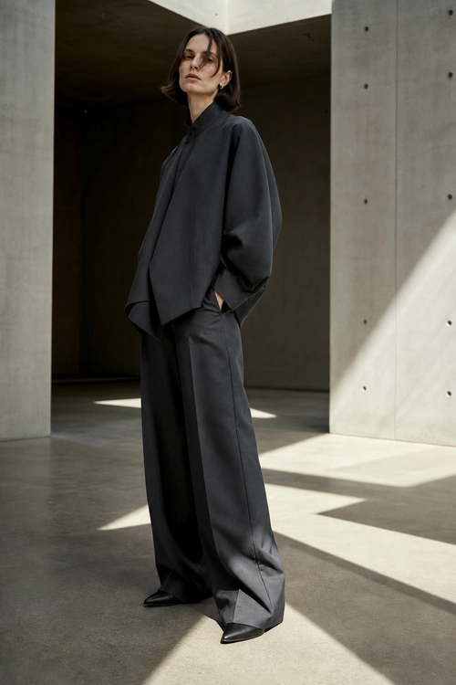 Monochrome Charcoal Tailoring A model wears an oversized charcoal long-sleeve top with wide-leg trousers and pointed black shoes.