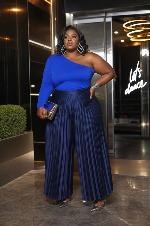 A woman wears a cobalt blue one-shoulder top with navy pleated wide-leg trousers, metallic pointed heels, geometric earrings, and a small metallic clutch.