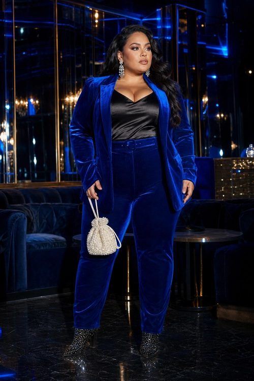 Cobalt Velvet Suit with Satin Top A cobalt blue velvet blazer and matching trousers styled with a black satin top, embellished ankle boots, drop earrings, and a small white beaded handbag.
