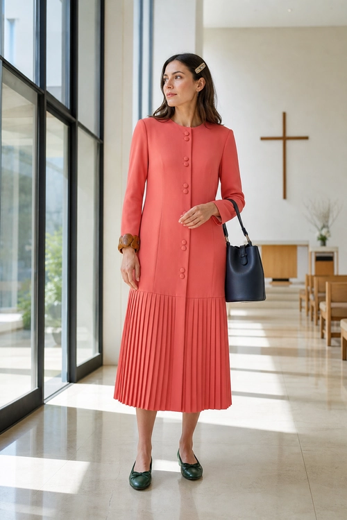 Coral Pleated Midi Dress Outfit Woman wearing a coral long-sleeve pleated midi dress with dark green flats and a dark handbag.