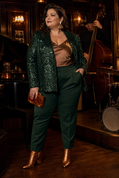 A polished outfit featuring a dark green sequin blazer, bronze satin top, matching trousers, metallic ankle boots, and a small clutch.