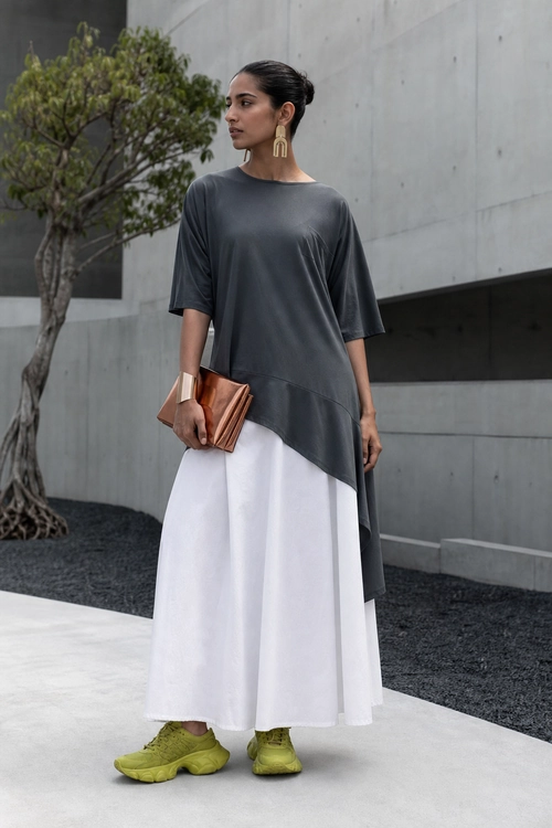 Asymmetric Gray Tunic with White Skirt A woman wears an asymmetrical charcoal gray tunic over a white skirt with lime green sneakers, a copper clutch, gold earrings, and a metallic cuff.