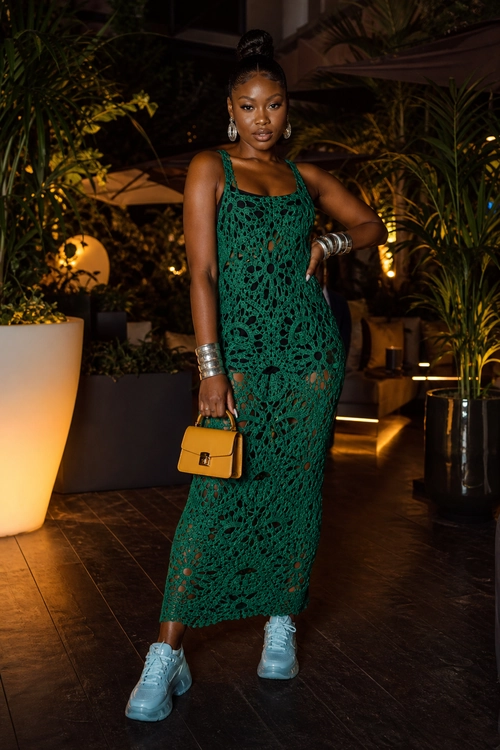Green Crochet Dress with Sneakers A woman wears a sleeveless emerald green crochet maxi dress with light blue chunky sneakers, a mustard yellow handbag, silver hoop earrings, and stacked bracelets.