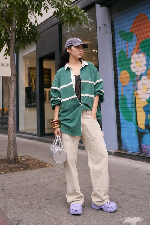 Street style outfit featuring a green striped overshirt, cream wide-leg pants, lavender cap and clogs, and a silver handbag.