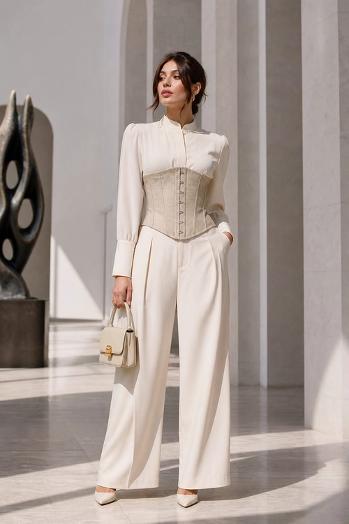 Ivory Blouse and Corset Trousers A woman wears an ivory blouse with a beige corset-style waist piece, wide-leg trousers, pointed heels, and a small structured handbag.