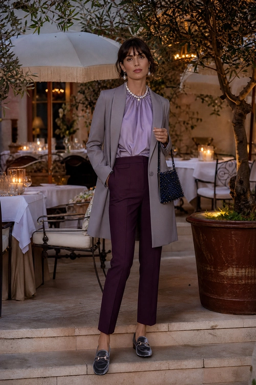 A tailored outfit featuring a gray long blazer, lavender blouse, burgundy trousers, black loafers, and a beaded handbag.