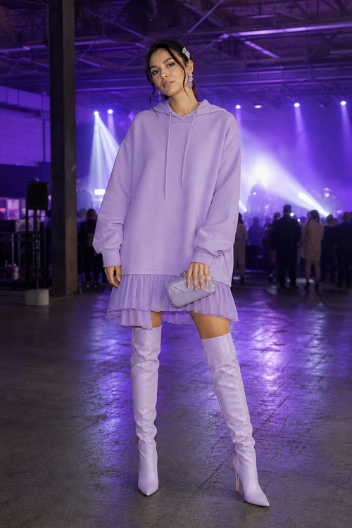 A lavender hoodie dress with a ruffled hem is styled with matching over-the-knee boots and a small clutch.