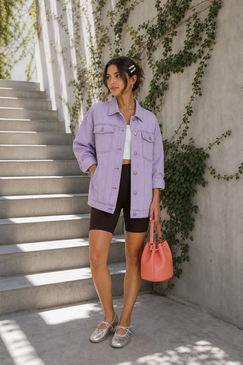 A casual outfit featuring a lavender jacket over a white cropped top, black fitted shorts, silver flats, and a coral handbag.