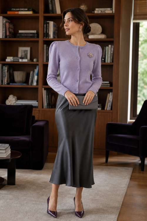 Lilac Cardigan and Satin Midi Skirt Outfit Woman wearing a lilac button-front cardigan with a brooch, gray satin midi skirt, gray clutch, and purple pointed-toe pumps.