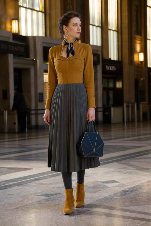 Mustard Blouse and Pleated Skirt Outfit A mustard long-sleeve blouse styled with a navy neck scarf, gray pleated midi skirt, dark tights, mustard ankle boots, and a geometric navy handbag.