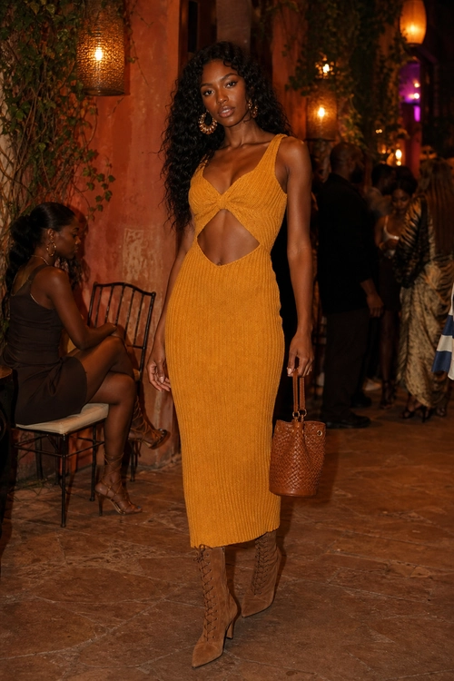 Mustard Cutout Midi Dress Outfit A woman wears a mustard ribbed cutout midi dress with brown knee-high boots, a woven handbag, and hoop earrings.