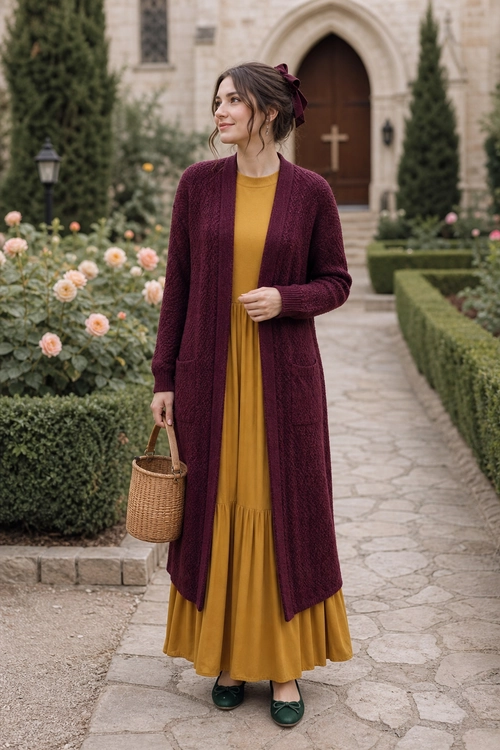 Mustard Dress with Burgundy Cardigan Woman wearing a mustard yellow dress, long burgundy cardigan, green flats, and carrying a woven basket handbag in a formal garden.