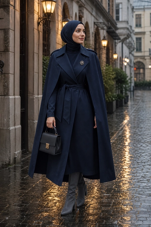 Navy Belted Cape Coat Outfit A woman wears a navy hijab and belted cape-style coat with a long dark dress, gray knee-high boots, and a structured black handbag.