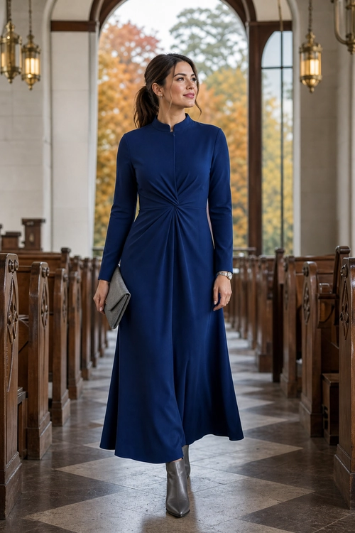 Navy Ruched Maxi Dress Outfit Woman wearing a long-sleeved navy maxi dress with a gathered waist, gray clutch, and gray ankle boots.