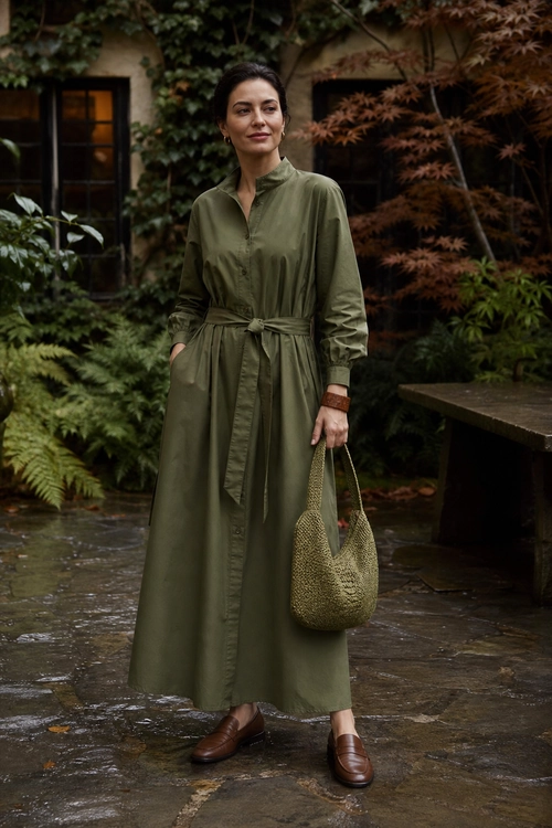 Olive Green Shirt Dress Outfit A woman wears an olive green belted shirt dress with brown loafers and a woven handbag.