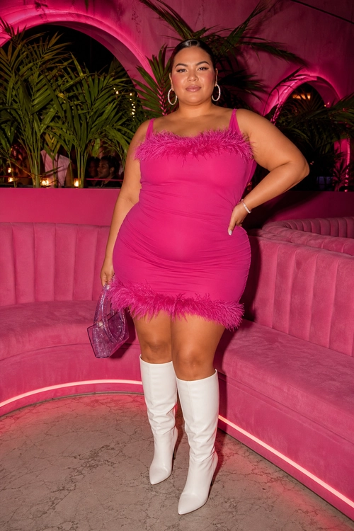 Pink Feather-Trim Mini Dress Outfit A woman wears a bright pink feather-trim mini dress with white knee-high boots, hoop earrings, and a small glitter handbag.