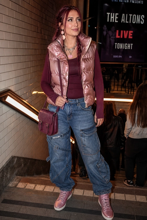 A fashion outfit featuring a metallic pink puffer vest over a burgundy top, baggy blue cargo jeans, pink high-top sneakers, and a matching crossbody bag.