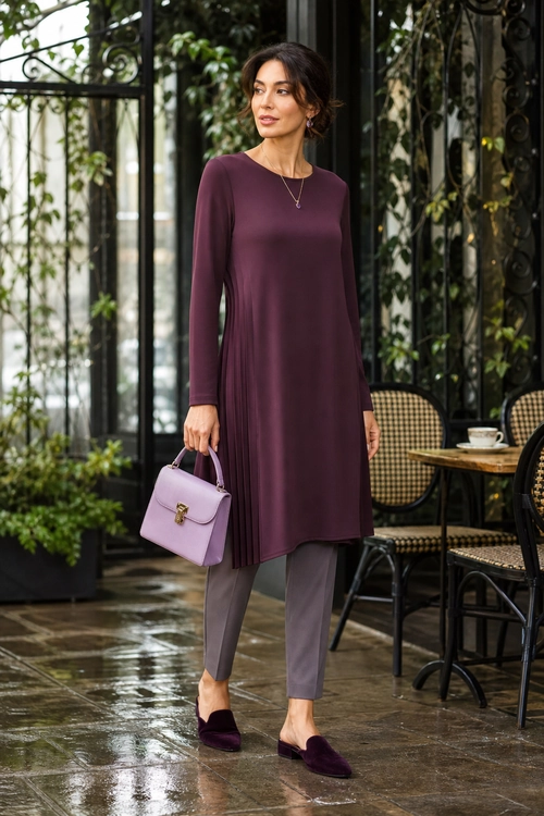 Plum Tunic Dress Outfit A woman wears a long-sleeve plum tunic dress with gray tapered trousers, dark plum flats, and a lavender handbag.