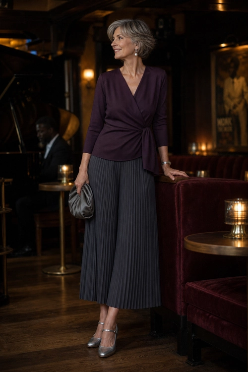 Woman wearing a plum wrap top with a charcoal pleated midi skirt, metallic heels, a clutch, drop earrings, and a wrist accessory.