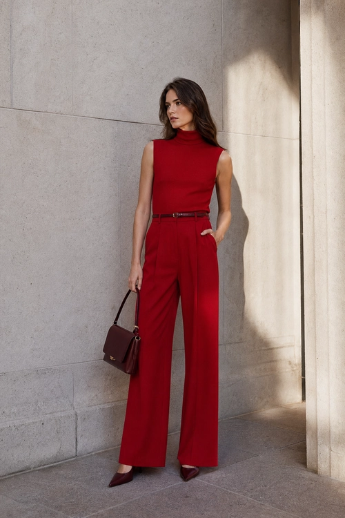 Red Sleeveless Top and Wide-Leg Trousers A woman wears a red sleeveless high-neck top with matching wide-leg trousers, a slim belt, burgundy pointed shoes, and a burgundy handbag.