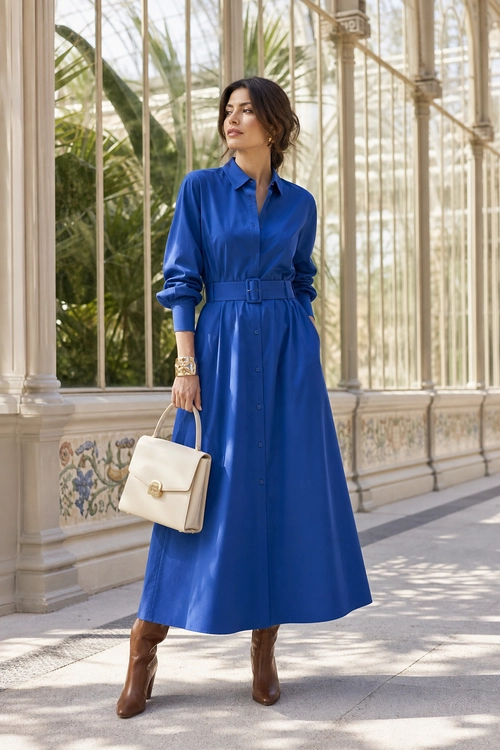 Royal Blue Belted Shirt Dress A woman wears a royal blue belted shirt dress with brown knee-high boots and carries a structured cream handbag.