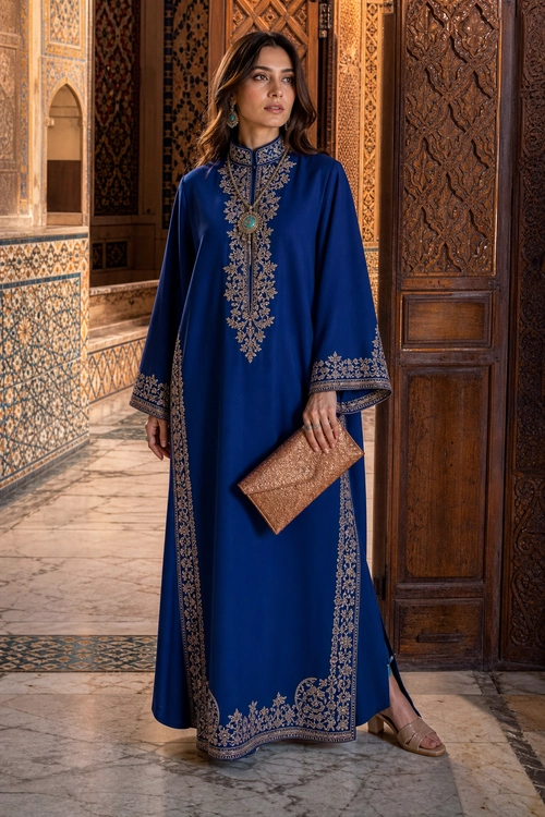 Embroidered Royal Blue Kaftan Woman wearing a floor-length royal blue kaftan with ornate metallic embroidery, a bronze clutch, earrings, and flat sandals.