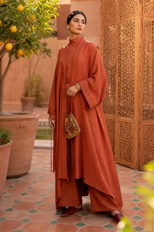 Rust Layered Traditional Outfit A model wears a flowing rust-colored layered tunic with matching wide-leg trousers, burgundy shoes, gold bangles, and a small floral pouch.