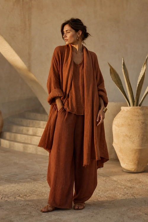 Rust Layered Wide-Leg Outfit A person wears a rust-colored long open layer over a matching top and wide-leg trousers with flat sandals.