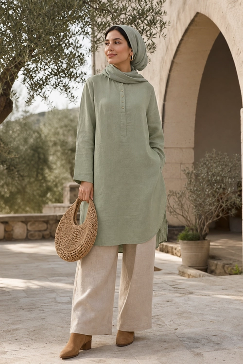 Sage Tunic and Wide-Leg Trousers Woman wearing a sage green long-sleeved tunic with a matching headscarf, cream wide-leg trousers, brown shoes, and a woven handbag.