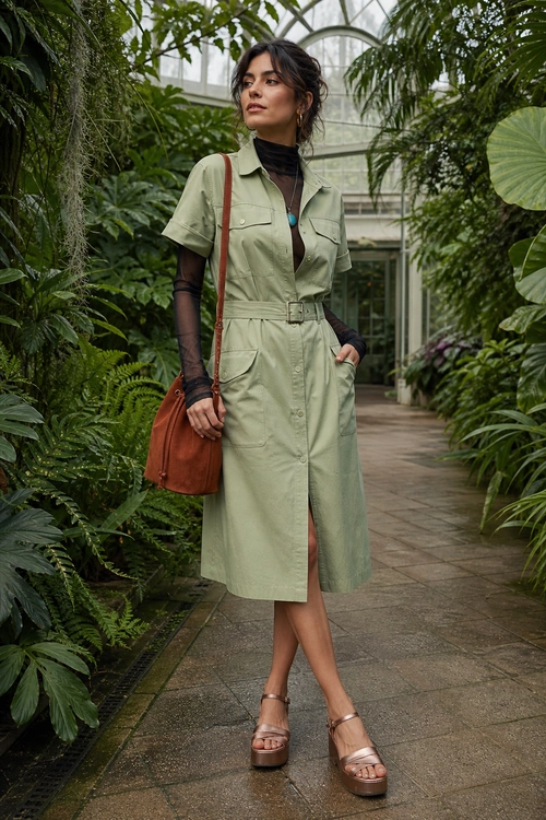 A sage green belted utility shirt dress layered over a black sheer top, styled with a brown shoulder bag and tan platform sandals.