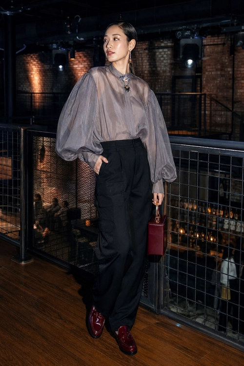 A sheer taupe blouse with voluminous sleeves is styled with black cargo trousers, burgundy loafers, and a matching handbag.
