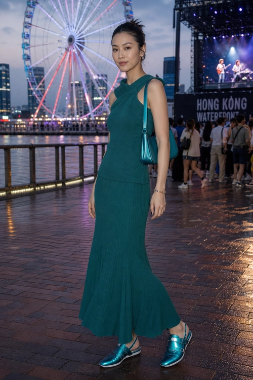 A woman wears a teal sleeveless cutout maxi dress with a matching shoulder bag and metallic platform sandals.