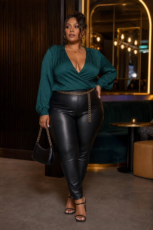 A teal long-sleeve wrap top styled with black leather-look pants, a gold chain belt, a black handbag, and black strappy heels.