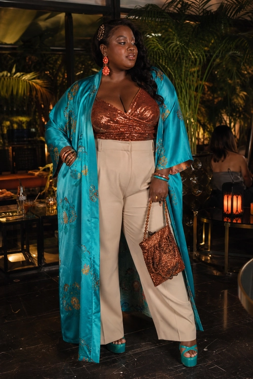 A fashion outfit featuring a turquoise patterned kimono, bronze sequin wrap-style top, cream wide-leg trousers, turquoise platform sandals, and a beaded handbag.