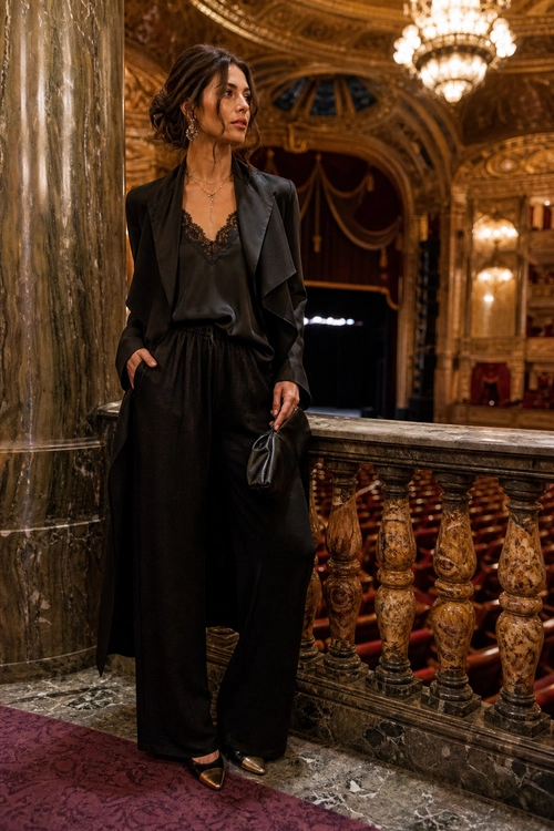 Elegant Black Satin Evening Look A woman wears a black blazer, lace-trim satin camisole, wide-leg trousers, pointed shoes, and carries a small black handbag.