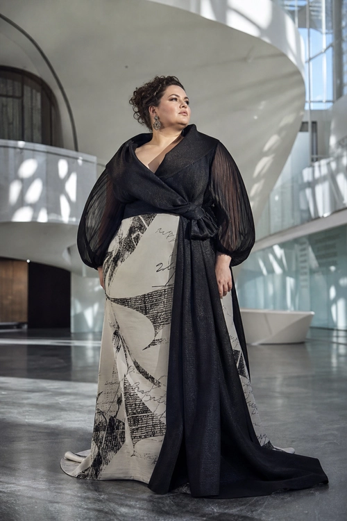 Black Wrap Top with Printed Maxi Skirt A woman wears a black sheer-sleeved wrap top with a long draped black overlay and a cream maxi skirt covered in abstract black prints.