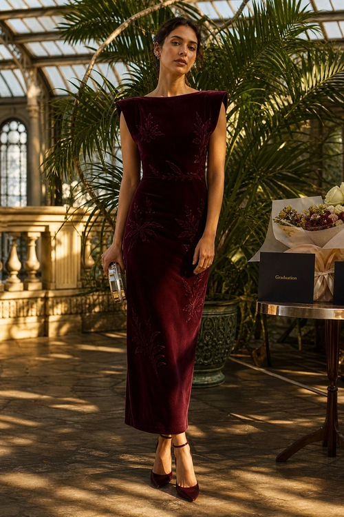 Burgundy Velvet Embroidered Dress Woman wearing a fitted burgundy velvet midi dress with floral embroidery, pointed heels, and holding a metallic clutch.