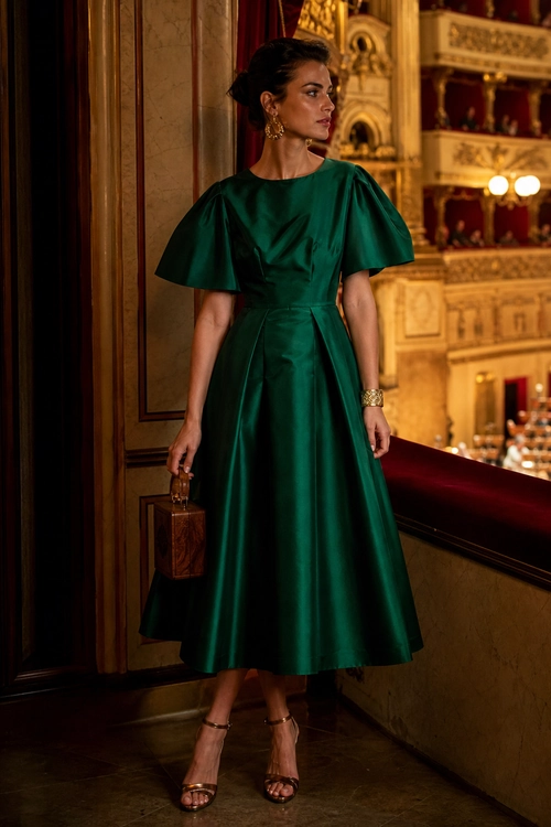 Woman wearing an emerald green satin dress with flared sleeves, strappy heels, gold earrings, a bracelet, and a small brown handbag.