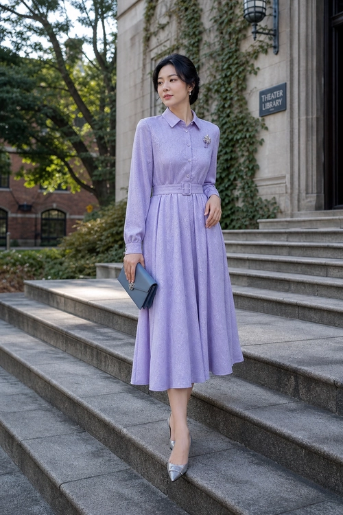 A woman wears a lavender long-sleeve belted midi dress with a brooch, blue clutch, and pointed silver heels on stone steps.