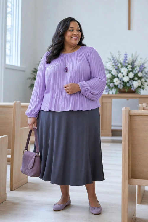 A woman wearing a lavender pleated long-sleeve blouse with a dark gray midi skirt, purple flats, a matching handbag, and a pendant necklace.