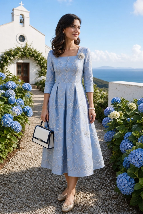 Woman wearing a light blue floral midi dress with a brooch, beige flats, and a white structured handbag.